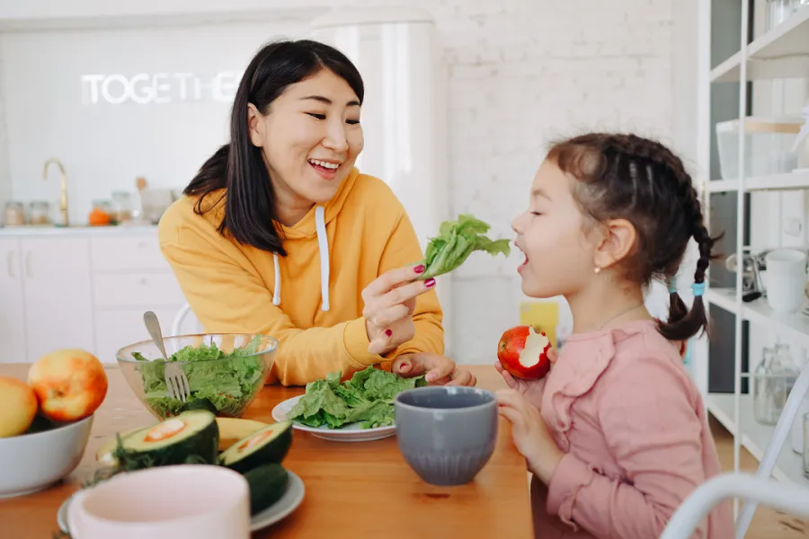 A lady feeding healthy vegetables to her girl child in the kitchen