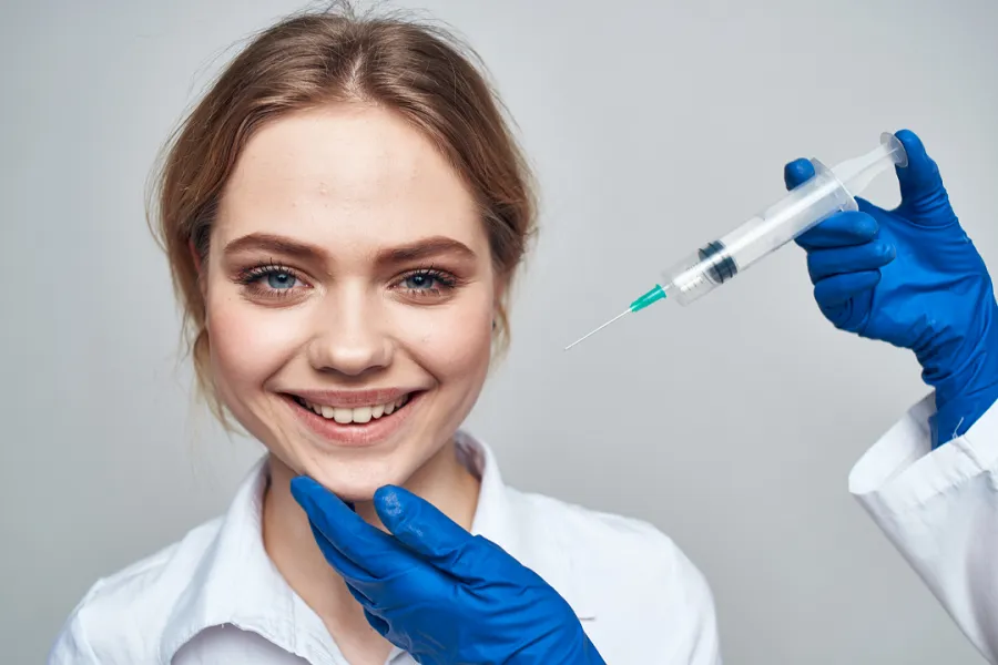 A lady smiling while doctor holding her chin and an injection