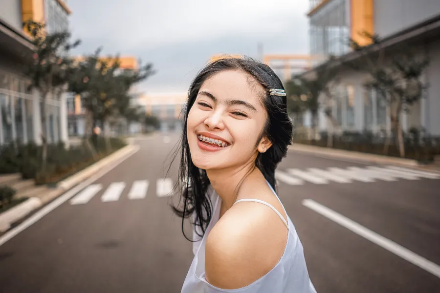 A lady with dental braces standing on the road and smiling at the camera