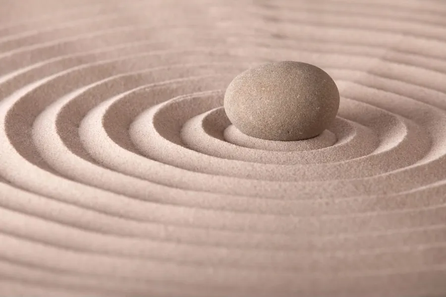 A single smooth stone rests in concentric raked lines of sand