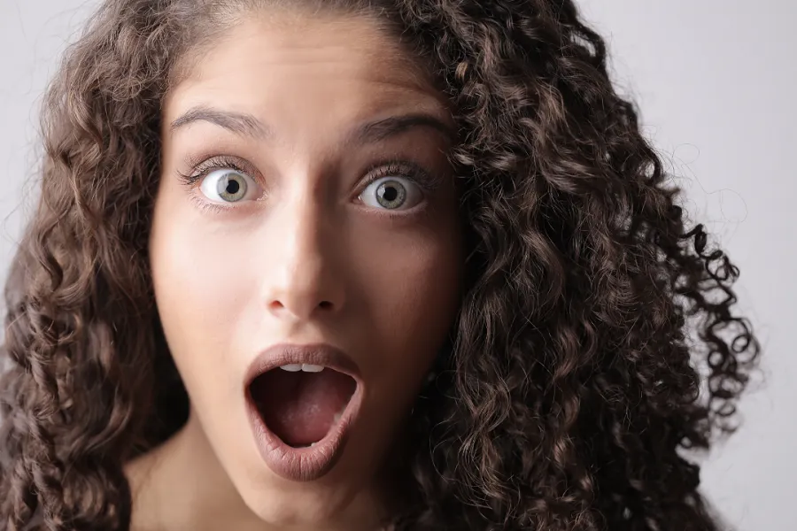 A woman with curly hair wearing a surprised expression on her face