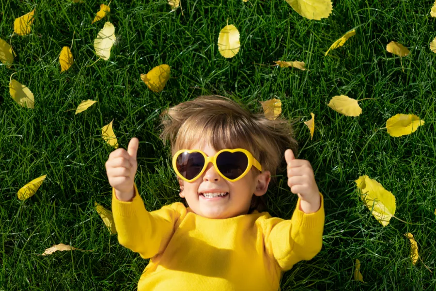 A young boy in sunglasses relaxing on grass with fallen leaves