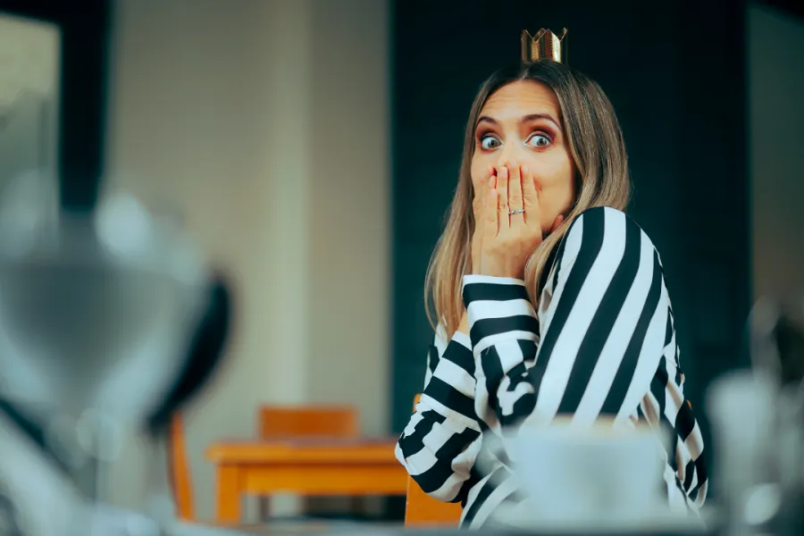 A shocked woman in a striped shirt with hands on her mouth