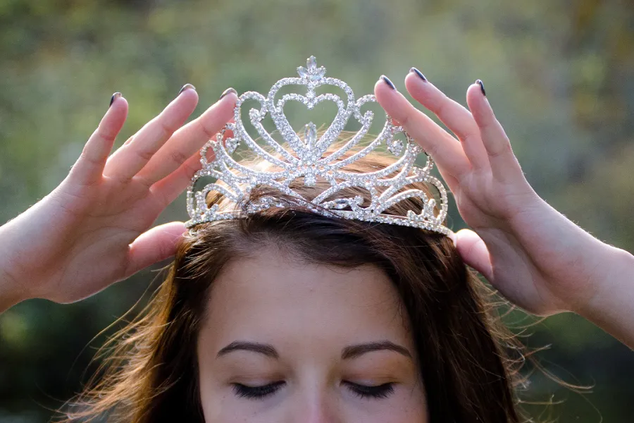 A young woman smiling while holding a tiara on her head