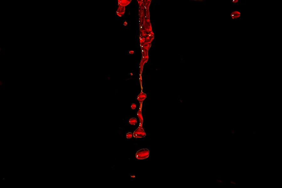 A series of red liquid droplets and splashes are suspended against a black background, creating a visually striking contrast