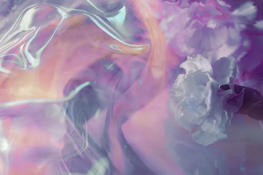 A close-up abstract image featuring soft, dreamy swirls of pink, purple, and white hues with hints of a delicate white flower in the background