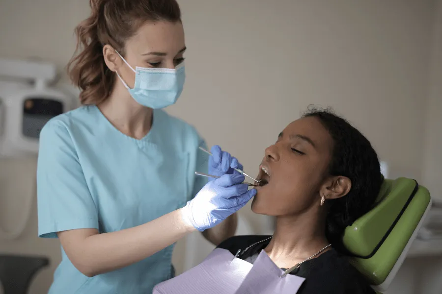 A dentist wearing a mask and gloves examines a patient's teeth using dental tools