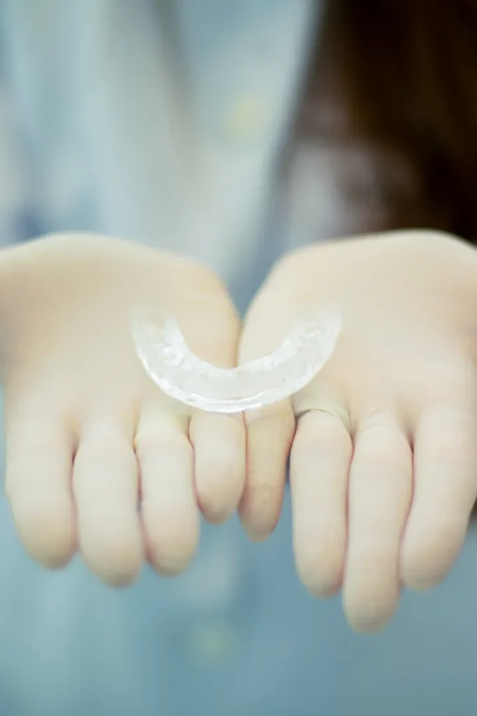 A person wearing white gloves holds a clear dental retainer in their open hands