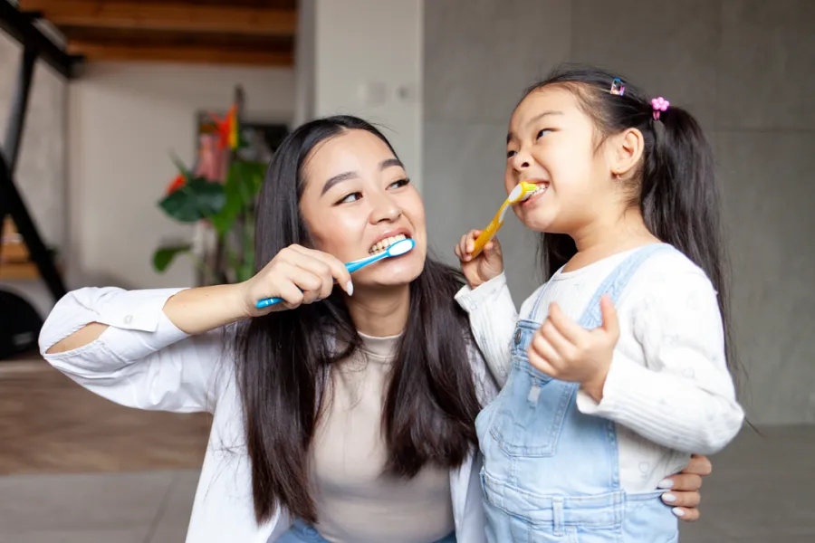 A woman and a young girl are brushing their teeth together