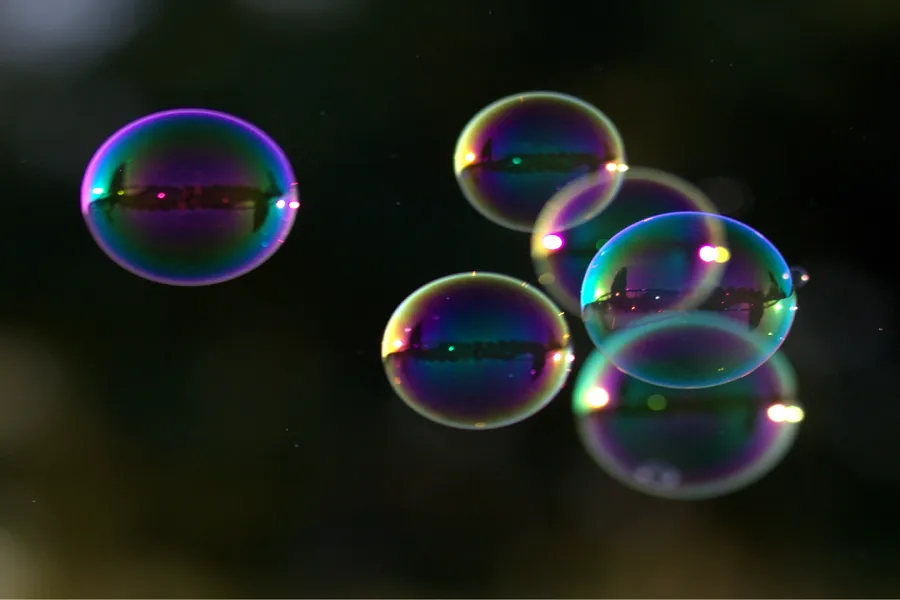 Several iridescent soap bubbles float against a dark, blurred background