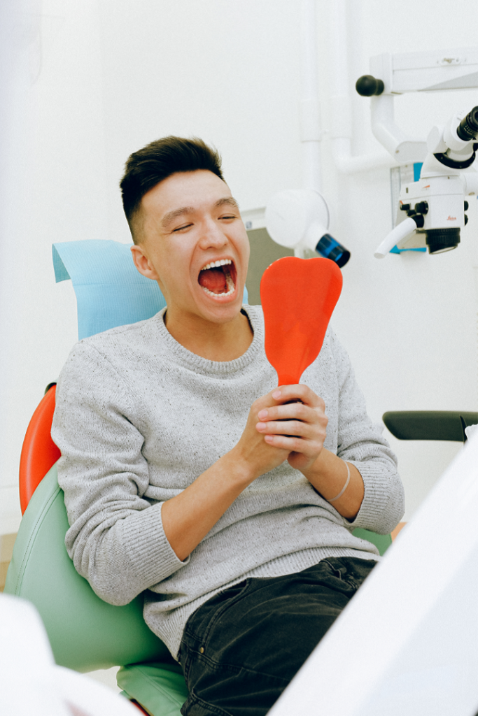 Person sitting in a dental chair holding a red dental mirror