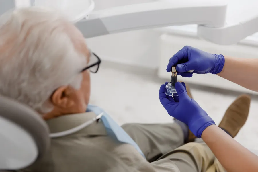 Dentist in gloves showing a patient a dental implant component