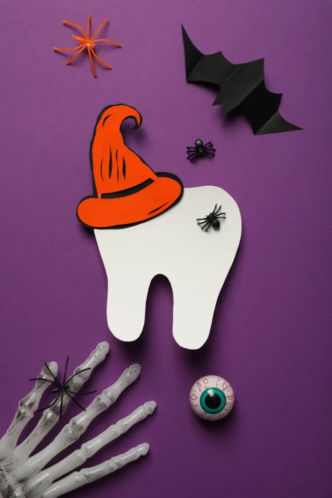 Halloween themed paper craft with tooth wearing a witch hat, spiders, bat, skeleton hand, and eyeball on purple background